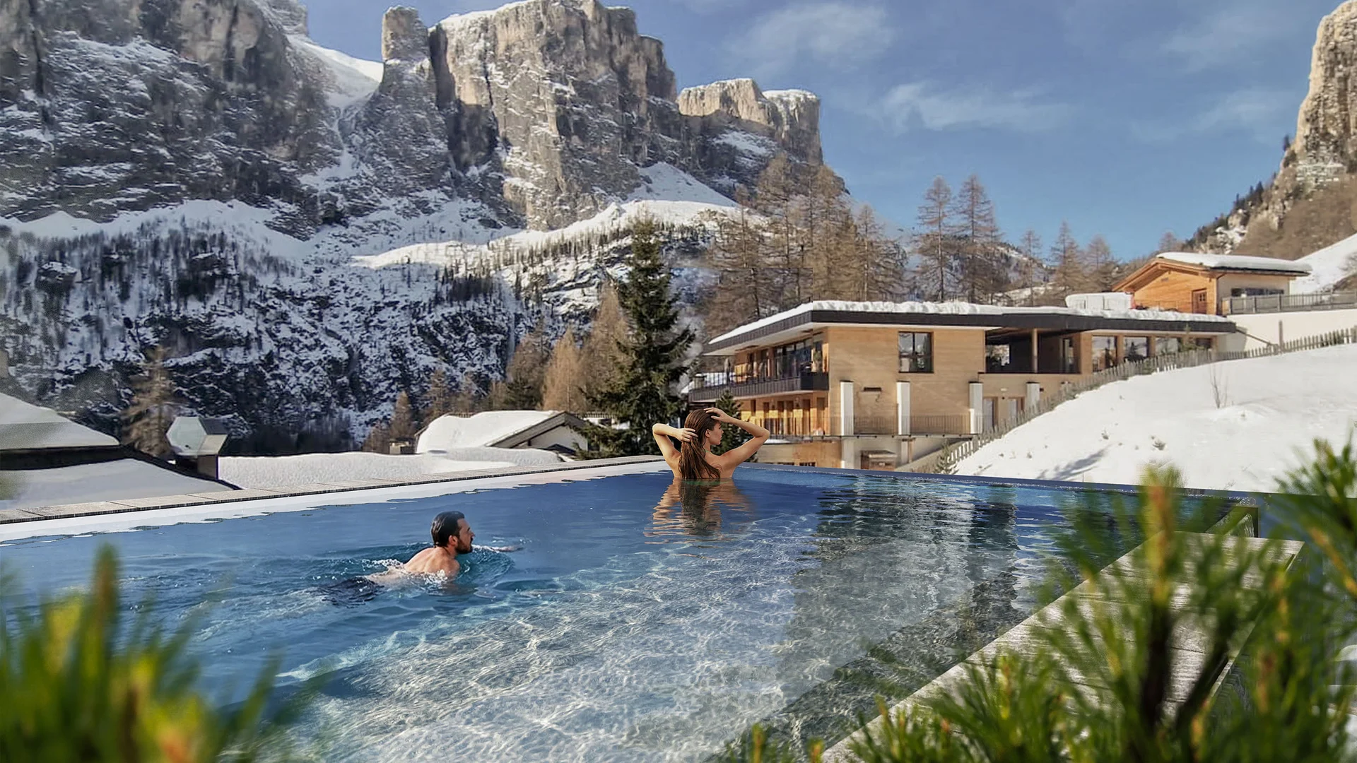 Zuhause auf Zeit im Hotel in Colfosco: Nature Hotel Delta Menschen schwimmen im Außenpool mit Blick auf schneebedeckte Berge und Gebäude