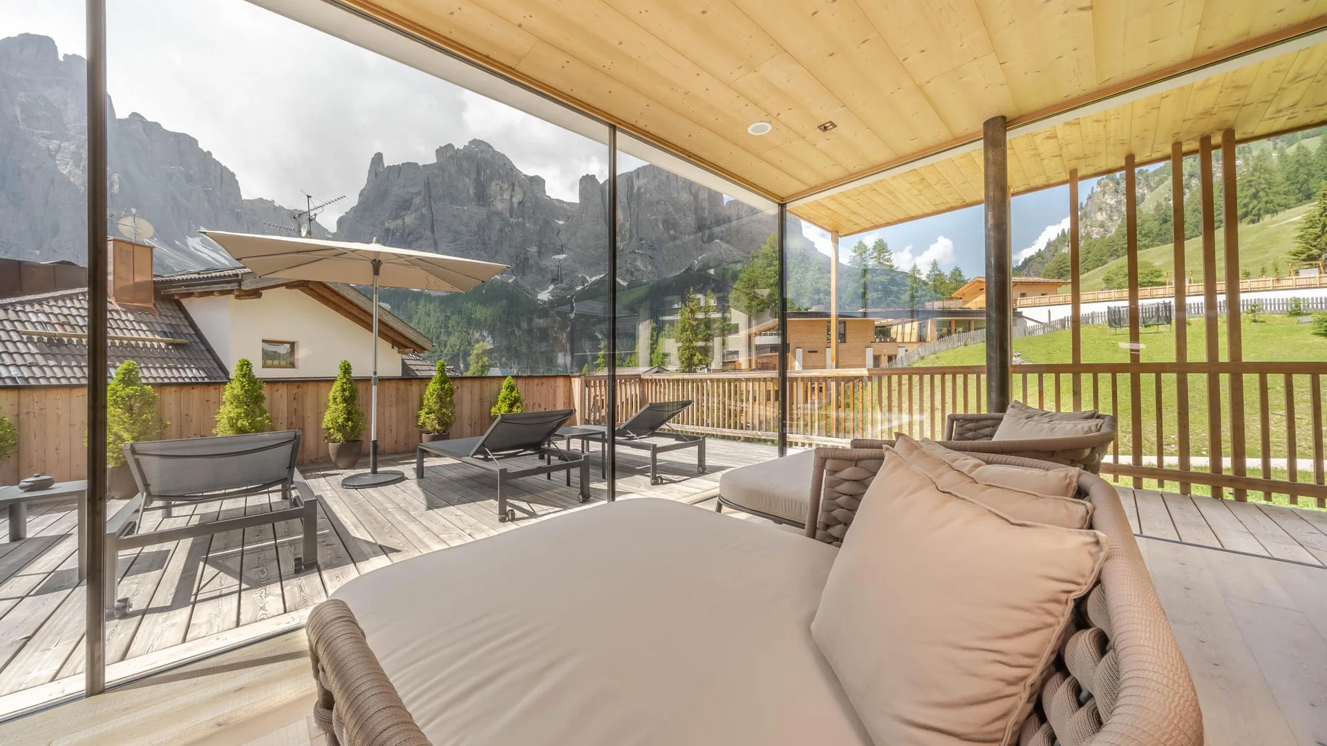 Zuhause auf Zeit im Hotel in Colfosco: Nature Hotel Delta Terrasse mit Liegestühlen und Bergblick hinter Glaswand