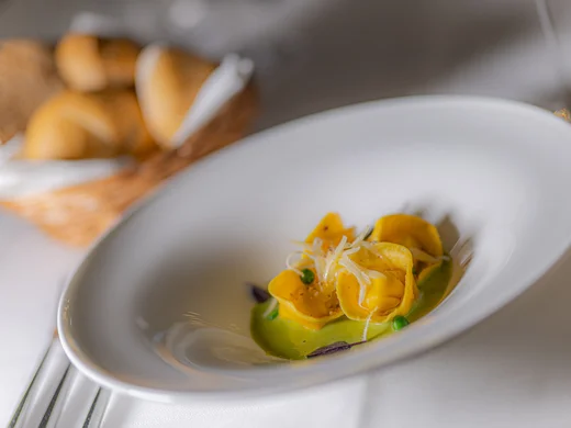 Zuhause auf Zeit im Hotel in Colfosco: Nature Hotel Delta Teller mit Tortellini auf grüner Sauce und Brotkorb im Hintergrund
