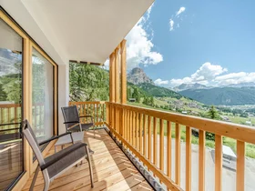 Zuhause auf Zeit im Hotel in Colfosco: Nature Hotel Delta Balkon mit Stühlen und Blick auf Berge und Tal bei klarem Himmel